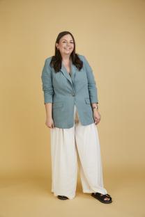 Woman in teal blazer and white pants smiling.