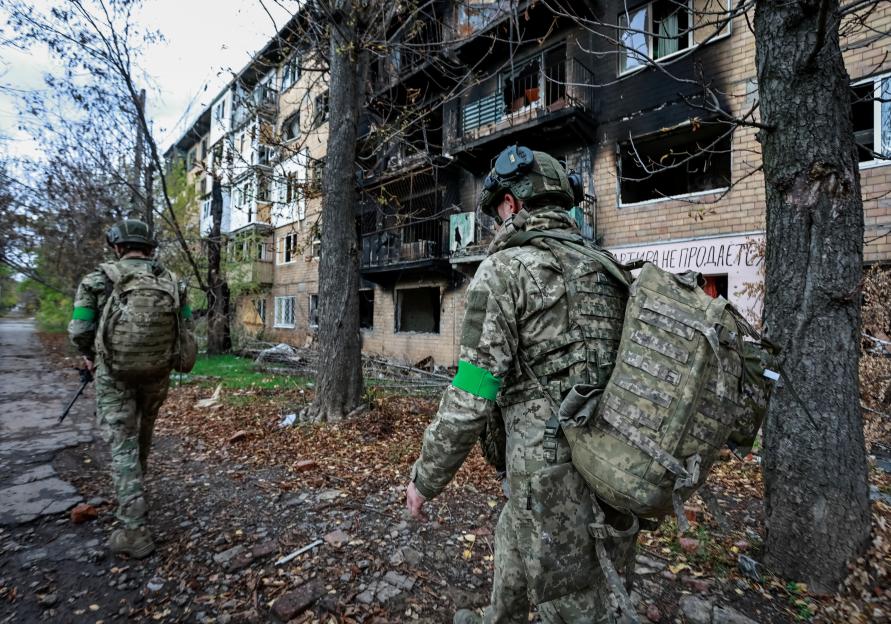 Ukrainian servicemen walk past a heavily damaged apartment building.
