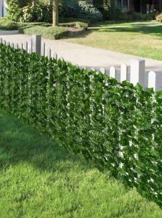 Artificial green leaf fence panels on a white picket fence.