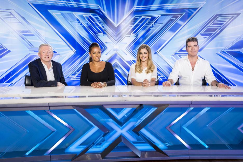 X-Factor judging panel with Louis Walsh, Mel B, Cheryl Fernandez-Versini, and Simon Cowell sitting at a desk with a blue X-Factor logo background.