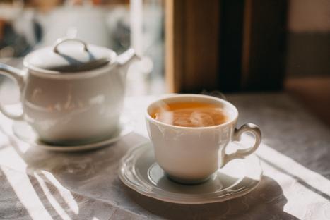 A cup of tea and teapot on a table in sunlight.