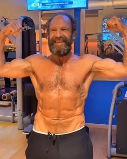Ralph Fiennes flexing his muscles in a gym.