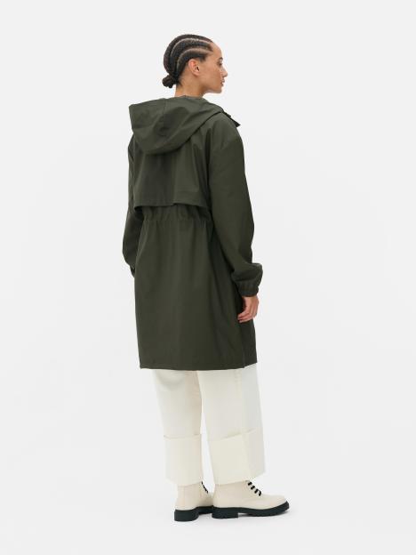 Woman in a hooded olive green raincoat, white pants, and cream-colored boots.