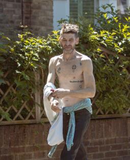 A tattooed man walking down the street, holding a shirt.