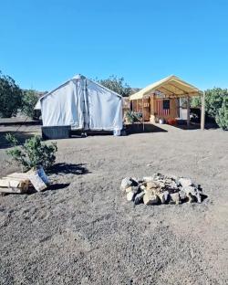 Large canvas tent and a covered structure on a desert campsite.