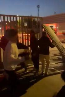 People moving a large panel near a gate at night.