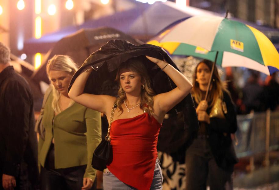 A young woman covers her head with a black leather jacket in the rain in Leeds.