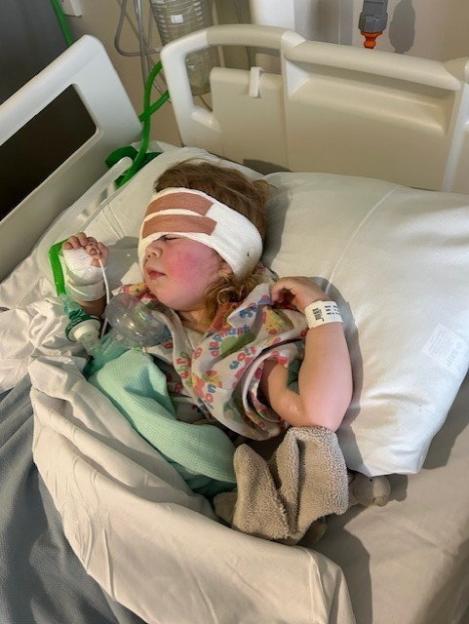 Young girl in hospital bed after eye removal surgery.