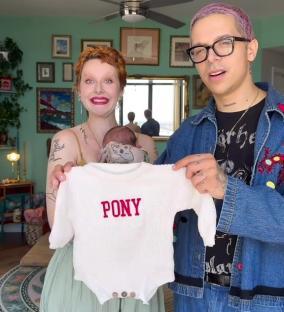 Parents holding their newborn baby, who is wearing a white sweater that says