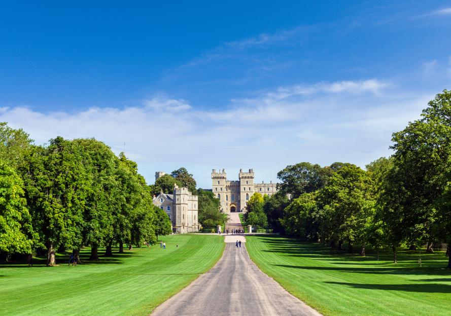Windsor Castle at the end of the Long Walk, surrounded by green lawns and trees under a blue sky.