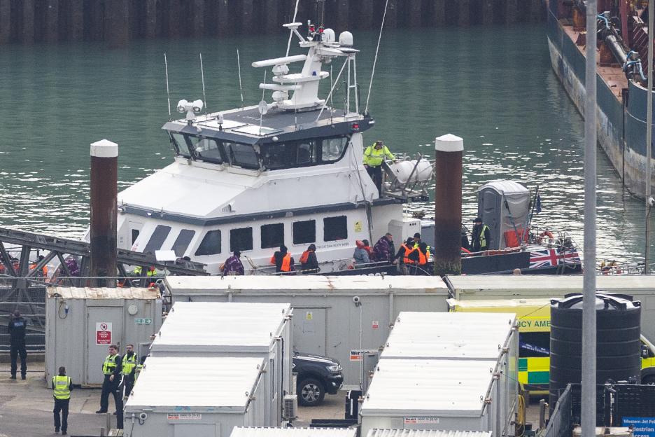 Migrants wearing life vests disembark from a vessel at Dover Marina, assisted by Border Force.