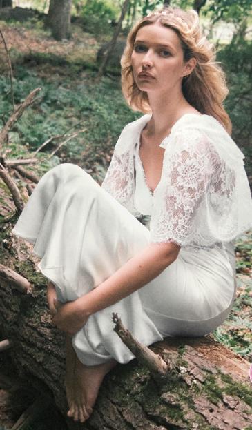 Apple Martin models a white lace and satin maxi dress from Self-Portrait, sitting on a log in a forest.