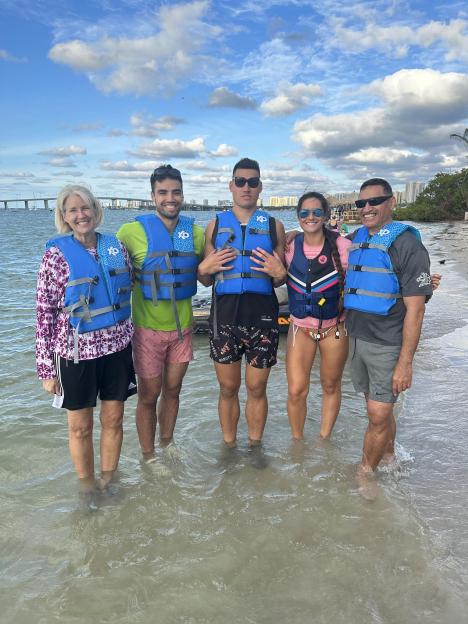 A family of five standing in shallow water wearing life vests.