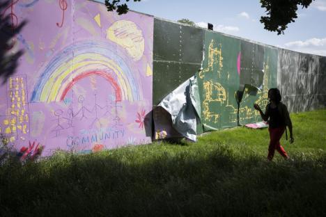 Person walking past a damaged festival screen with children's drawings.
