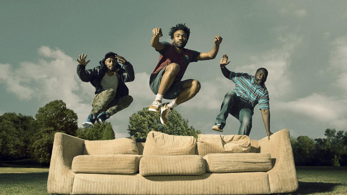 Keith Stanfield as Darius, Donald Glover as Earnest Marks, and Brian Tyree Henry as Alfred Miles, jumping above a couch in a park.
