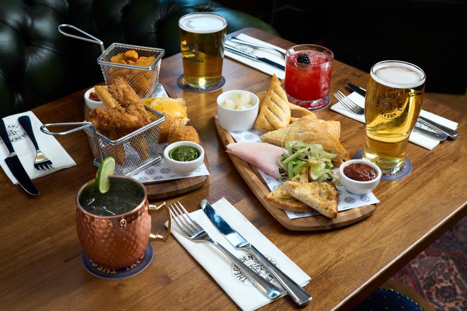 Platters of food and drinks from The Golden Flake Tavern, a Greggs pub, on a wooden table.