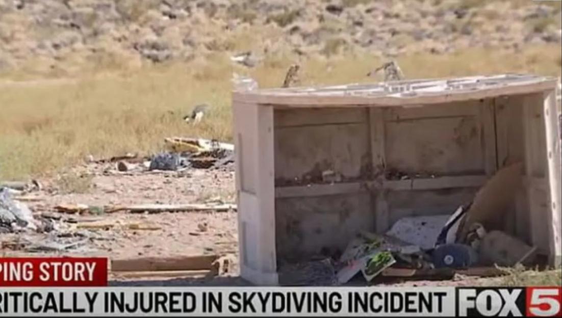 Debris from a skydiving incident scattered on the ground with a broken wooden structure in the foreground.