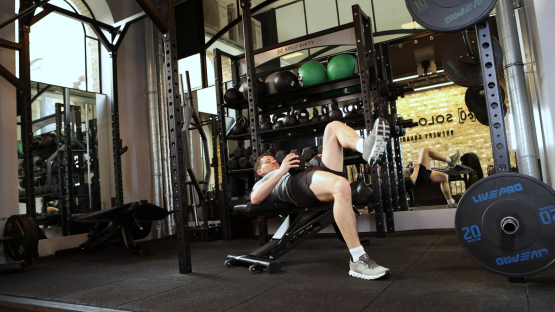 Man doing leg raises with dumbbells in a gym.