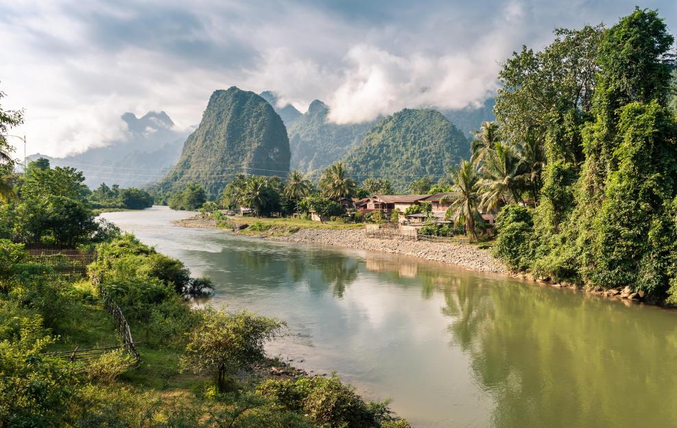 Nam Song River in Vang Vieng, Laos, with houses and mountains.