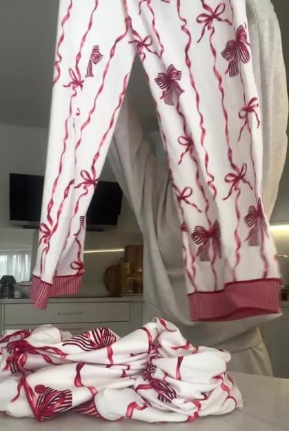 Person holding up white pajama bottoms with red ribbon and bow patterns.