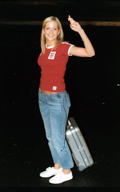 Kate Lawler from Big Brother 3, wearing an England shirt and holding up crossed fingers, with a suitcase at her feet.