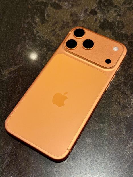An orange iPhone 17PM with three camera lenses and an Apple logo on the back.