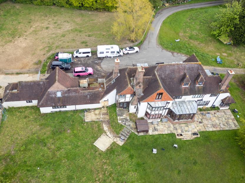 Aerial view of a large house with multiple vehicles parked on the driveway.