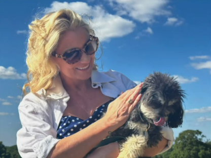 Woman holding a small dog outdoors.
