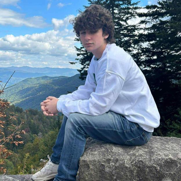 Elijah Heacock sitting on a rock with a mountain range in the background.