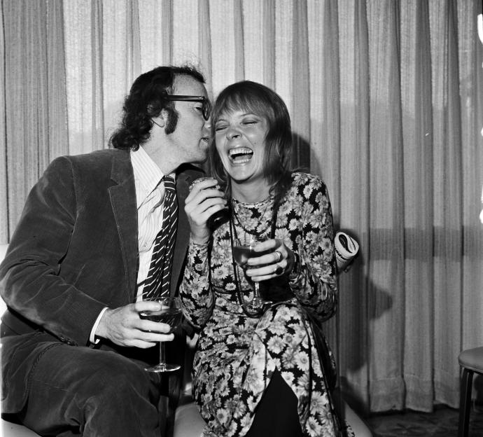 Woody Allen whispers into Diane Keaton's ear as she laughs while holding a drink.