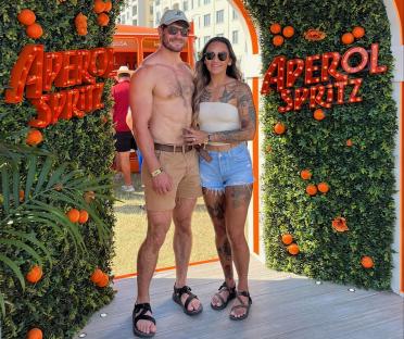 Couple posing in front of Aperol Spritz display at a music festival.