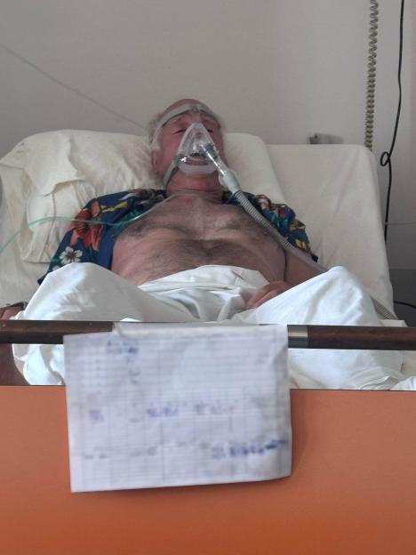 Man on ventilator in hospital bed.