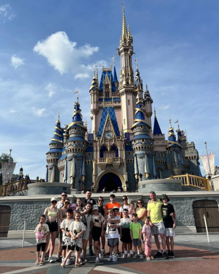 A large group of adults and children posing in front of Cinderella's Castle at Disney World.