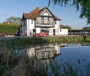 The Queens Head pub in West Bergholt, Essex, reflected in a pond.