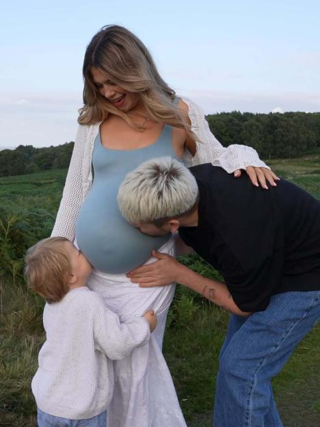 Pregnant woman with her toddler and partner kissing her baby bump.