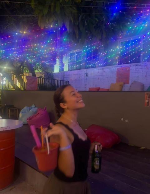 Woman holding a bucket of drinks and a beer bottle at a bar at night.
