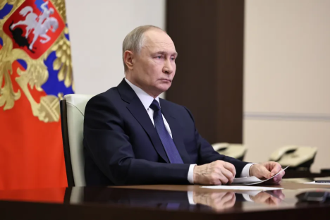 Vladimir Putin sitting at a table reviewing documents.