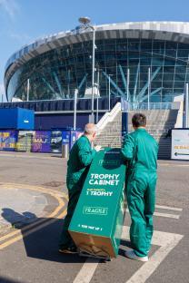 Two people in green uniforms moving a large box labeled 
