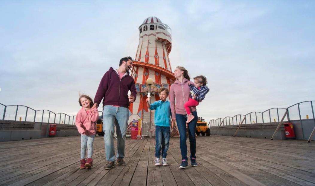 A family of four walking on a pier with an amusement ride in the background.