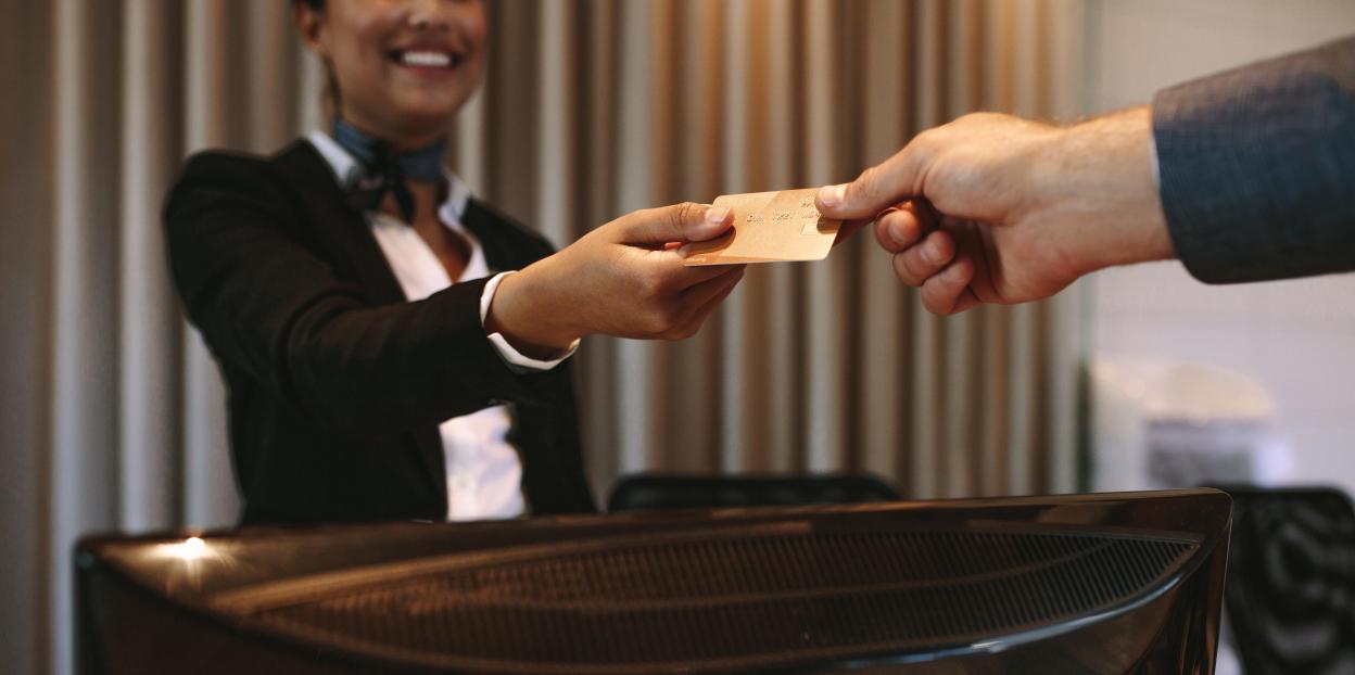 A businessman hands a credit card to a hotel receptionist.