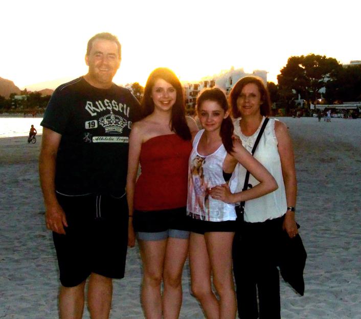 Photo of John Hunt with his wife and two daughters on a beach at sunset.