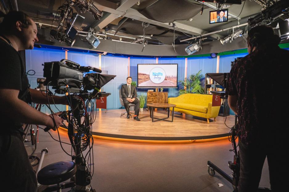 A television studio set with crew filming a male guest.