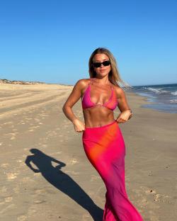 Woman in pink bikini and matching skirt on a beach.