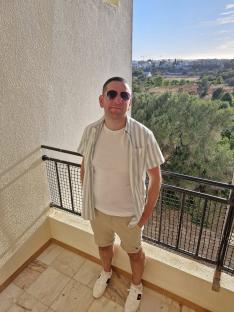 Man standing on a balcony wearing a striped shirt and shorts.