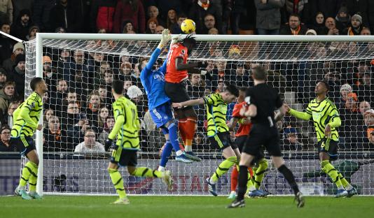 A soccer player heads the ball into the goal past the goalkeeper.