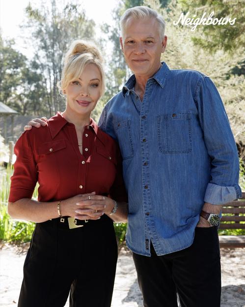 A man and woman stand together, arm in arm, in front of a blurred background. The text "Neighbours" is visible in the upper right corner.