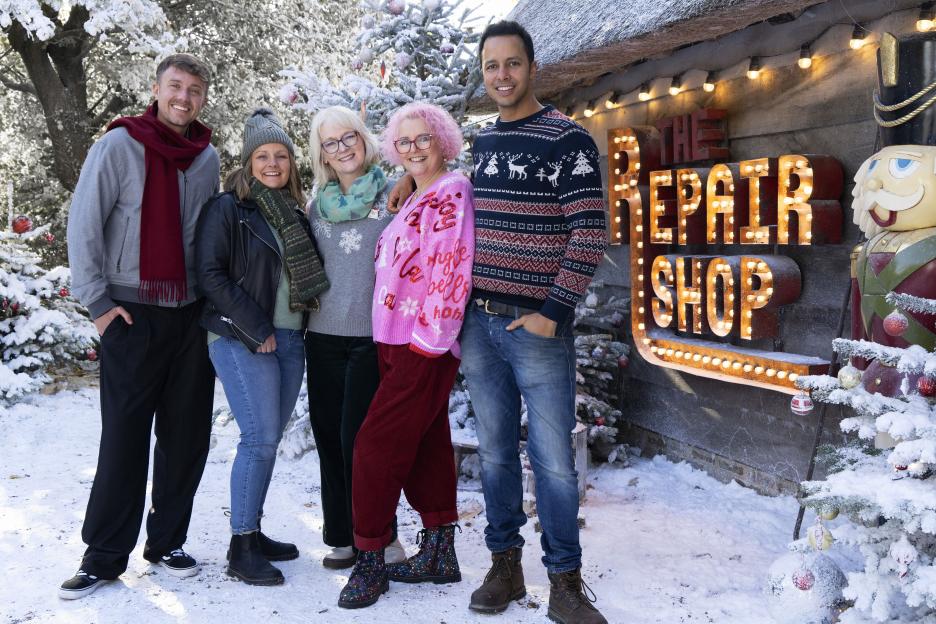 The Repair Shop Christmas special cast in front of a festive shop sign.