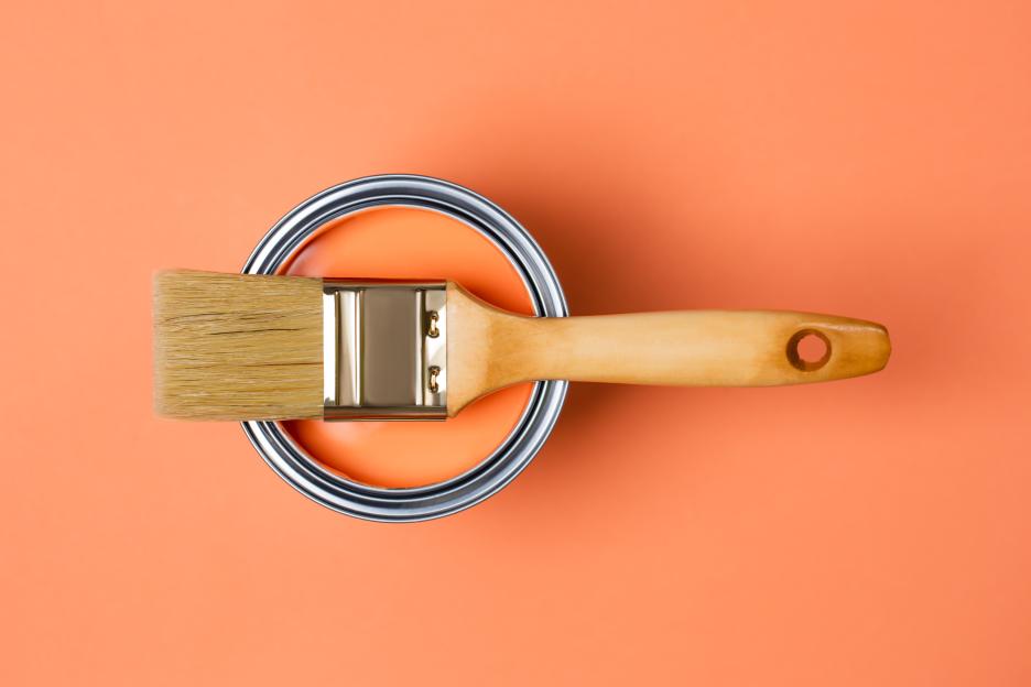 Paintbrush in a can of orange paint.