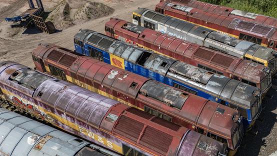 Aerial view of a dozen rusty diesel locomotives abandoned in a quarry.