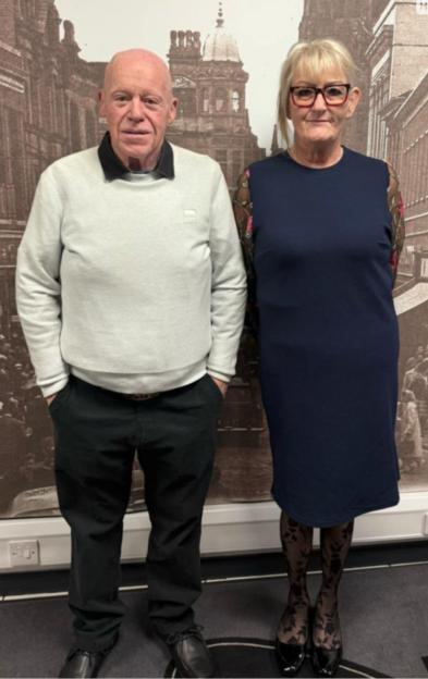 Photo of a man and woman standing in front of a historical photo.